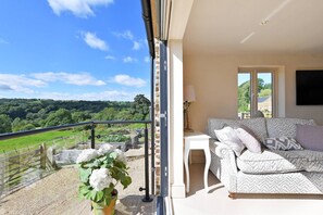Un balcone con vista su dolci colline verdi, un divano bianco con cuscini decorati e una pianta in vaso.