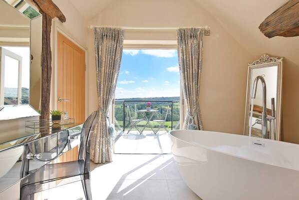 A modern bathroom with a large bathtub, a glass shower enclosure, and a view of a green landscape through the curtains. - Horseshoe House - Luxury Cottages (Dronfield)