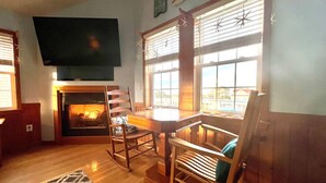 A cozy living room with a fireplace, wooden furniture, and large windows. - N3325-Oceanside, Nags Head, Saturday Check In, Private Pool! (Nags Head)