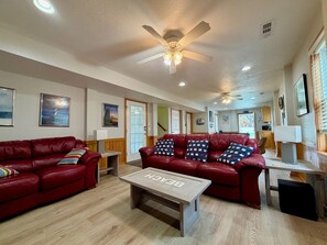 A spacious living room with red leather sofas, a wooden coffee table, ceiling fans, and framed pictures on the walls. - N3325-Oceanside, Nags Head, Saturday Check In, Private Pool! (Nags Head)
