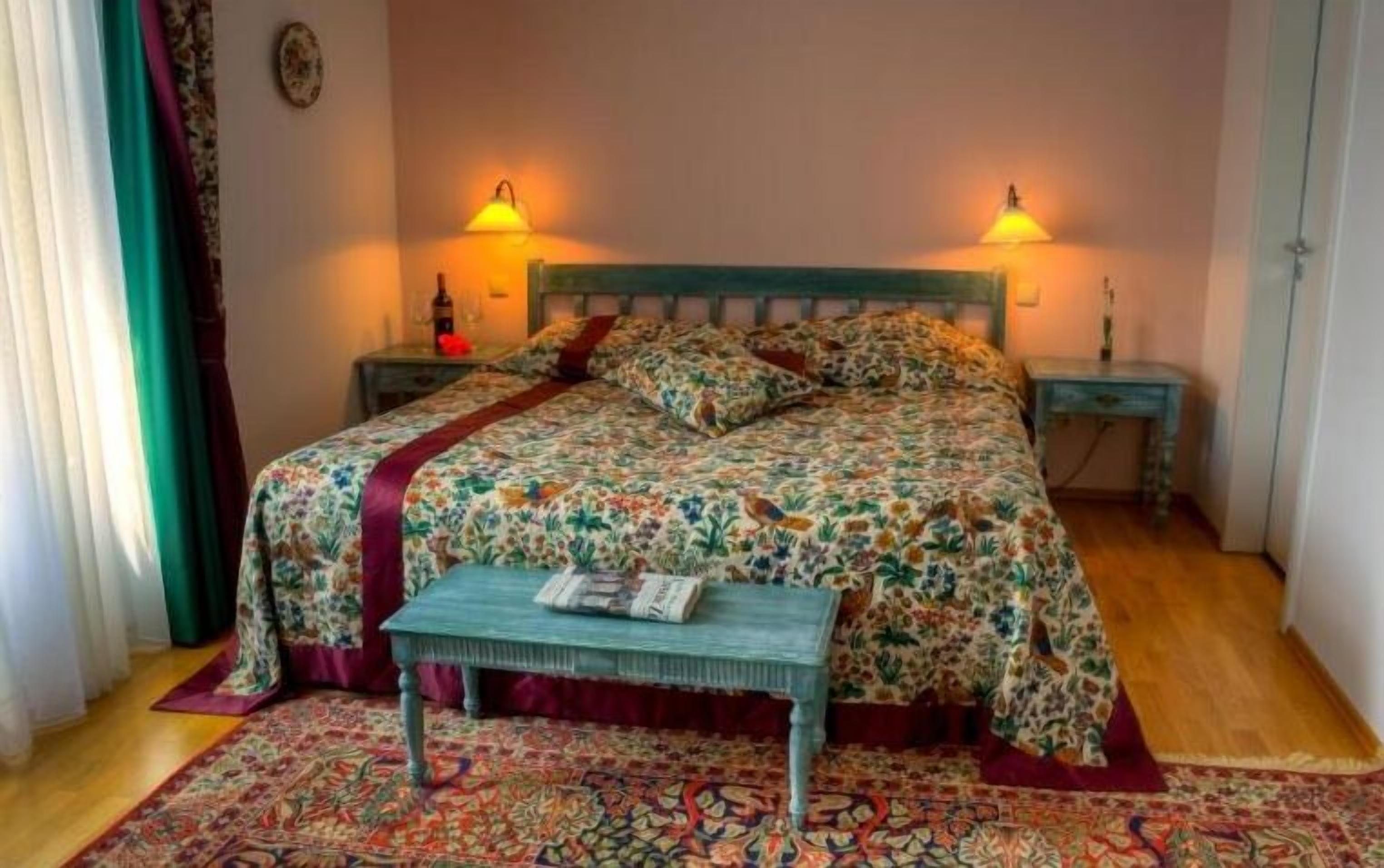 Un dormitorio con colcha estampada de flores, dos lámparas de noche, un banco de madera y un tapete con diseño.