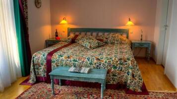 Un dormitorio con colcha estampada de flores, dos lámparas de noche, un banco de madera y un tapete con diseño.