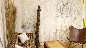 A room with a patterned wallpaper, a wooden sculpture, a zebra-patterned sofa, and a brown leather chair. - Hotel Henry (Erding)