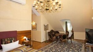 A bedroom with a bed, a chandelier, a dining table with chairs, and a TV. - Hotel Henry (Erding)