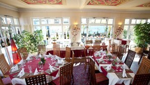 A restaurant with multiple dining tables set with red tablecloths and white napkins, surrounded by wooden chairs. - Hotel Henry (Erding)