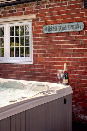 Un jacuzzi con una botella de champán Moët & Chandon y dos copas, frente a un muro de ladrillo con un letrero que dice 'Bikes and Fruits'.