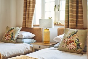 Un dormitorio con dos camas, una mesita de noche, una lámpara y cortinas.