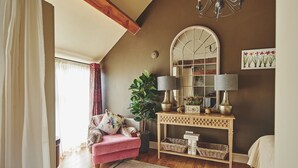 Een gezellige woonkamer met een roze fauteuil, een houten console tafel met lampen, een grote spiegel en een plant in pot.