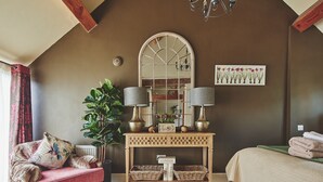Een gezellige slaapkamer met een grote spiegel, twee lampen, een potplant, een decoratieve console en een bed met een groene deken.