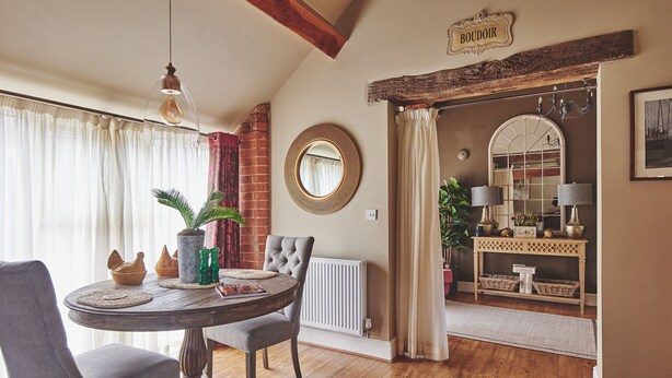 Een eetgedeelte met een ronde tafel, stoelen en een hanglamp. Aan de muur hangt een spiegel en een bord met de tekst 'BOUDOIR'.