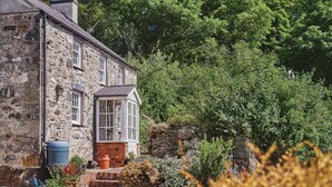 A stone building with a bay window, a brick entrance, and a garden with various plants.