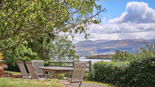 A wooden bench and table set on a stone pathway, overlooking a lake and mountains.