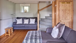 A cozy living room with a grey sofa, a small wooden table, and a staircase leading to a wooden door.