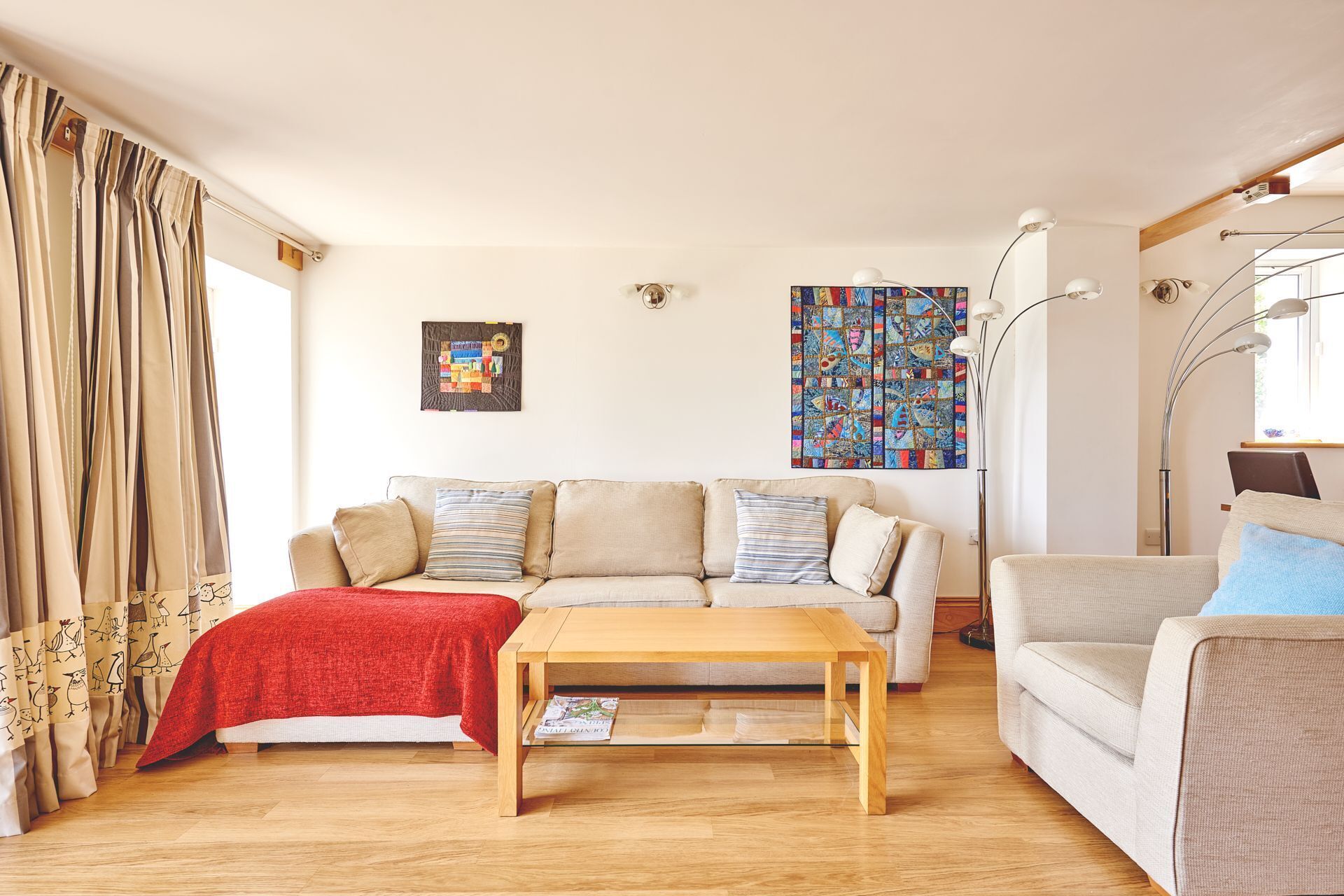 A living room with a sofa, a coffee table, and a chair. There are curtains, a painting, and a lamp.