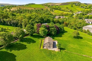 An aerial view of a rural landscape with a stone building surrounded by lush green fields and trees. - Meadow Barn - Luxury Cottages (Sowerby Bridge)