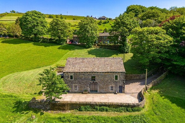 A stone house with a tiled roof, surrounded by lush greenery and a small pond. - Meadow Barn - Luxury Cottages (Sowerby Bridge)