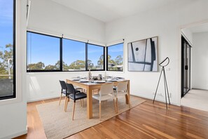 Ein moderner Essraum mit einem Holztisch, Stühlen und Blick durch große Fenster.