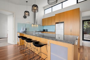A modern kitchen with a central island, bar stools, stainless steel appliances, and pendant lighting.