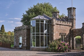 A historic building with a conservatory, stone walls, and a large tree in the background. - Victoria Lodge - Luxury Cottages (Leominster)