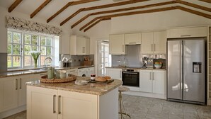 A kitchen with white cabinets, a stainless steel refrigerator, and a window with a view of greenery. - Flock Cottage -  a cottage that sleeps 8 guests  in 4 bedrooms (Pudleston)