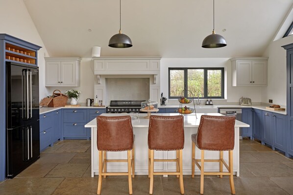 A kitchen with a central island, bar stools, a stove, and pendant lights.