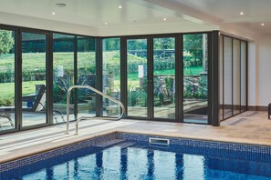 A swimming pool with a glass enclosure, offering a view of a landscaped garden.