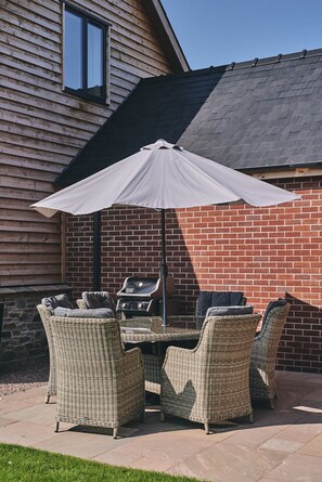 A patio with wicker furniture, a grill, and a large umbrella. - The Byre - Luxury Cottages (Leominster)