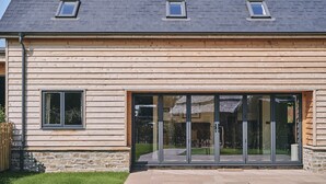 A modern building with a sloped roof, large glass doors, and wooden siding. - The Byre - Luxury Cottages (Leominster)