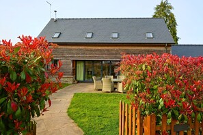 Een huis met schuin dak, een terras met tuinmeubilair en een verzorgd gazon.