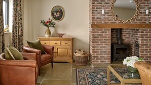 A living room with a fireplace, leather sofa, wooden cabinet, and a vase of flowers. - The Byre - Luxury Cottages (Leominster)