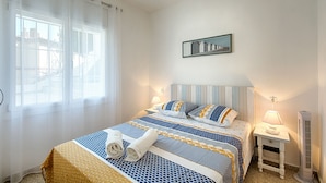 Een slaapkamer met een bed, twee nachtkastjes, een aan de muur hangend schilderij en een raam met gordijnen.