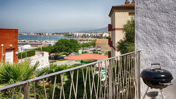 Een balkon met uitzicht op een jachthaven, een barbecue en een gebouw met een gestructureerde muur.