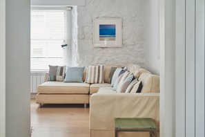 Relax in this inviting living room with a comfortable sofa, framed beach scene, and warm wooden floor.