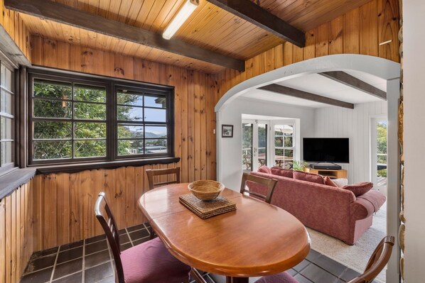 A wooden interior with a dining area, a sofa, and a television in the background.