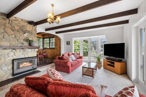 A cozy living room with a stone fireplace, a red sofa, a television, and a wooden ceiling.