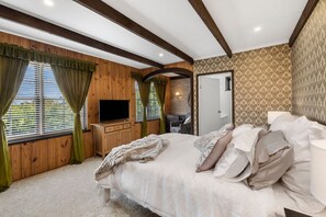 A bedroom with a bed, a TV, wooden walls, and a patterned wallpaper.