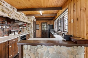 A kitchen with a stone backsplash, wooden cabinets, and a large window.