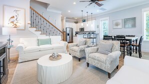 A spacious living room with a white sofa, patterned armchairs, a coffee table, and a dining area with wooden chairs and a table. - Screened Porch ~ Golf Cart ~ Community Pool (Miramar Beach)