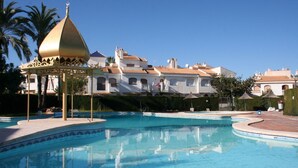 Una piscina con un pabellón, palmeras y un edificio con tejados de tejas.