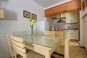A compact kitchen with wooden cabinets, a white refrigerator, and a glass dining table with chairs. - 029 - Bochiot 001 - comfortHOLIDAYS (Santa Pola)