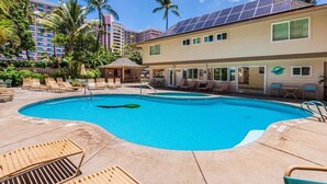 Ein Schwimmbecken mit Liegestühlen, Sonnenschirm und einem Gebäude mit Solaranlage.