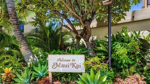 Ein Schild empfängt Besucher im Maui Kai, umgeben von üppiger tropischer Vegetation und einer Palme.