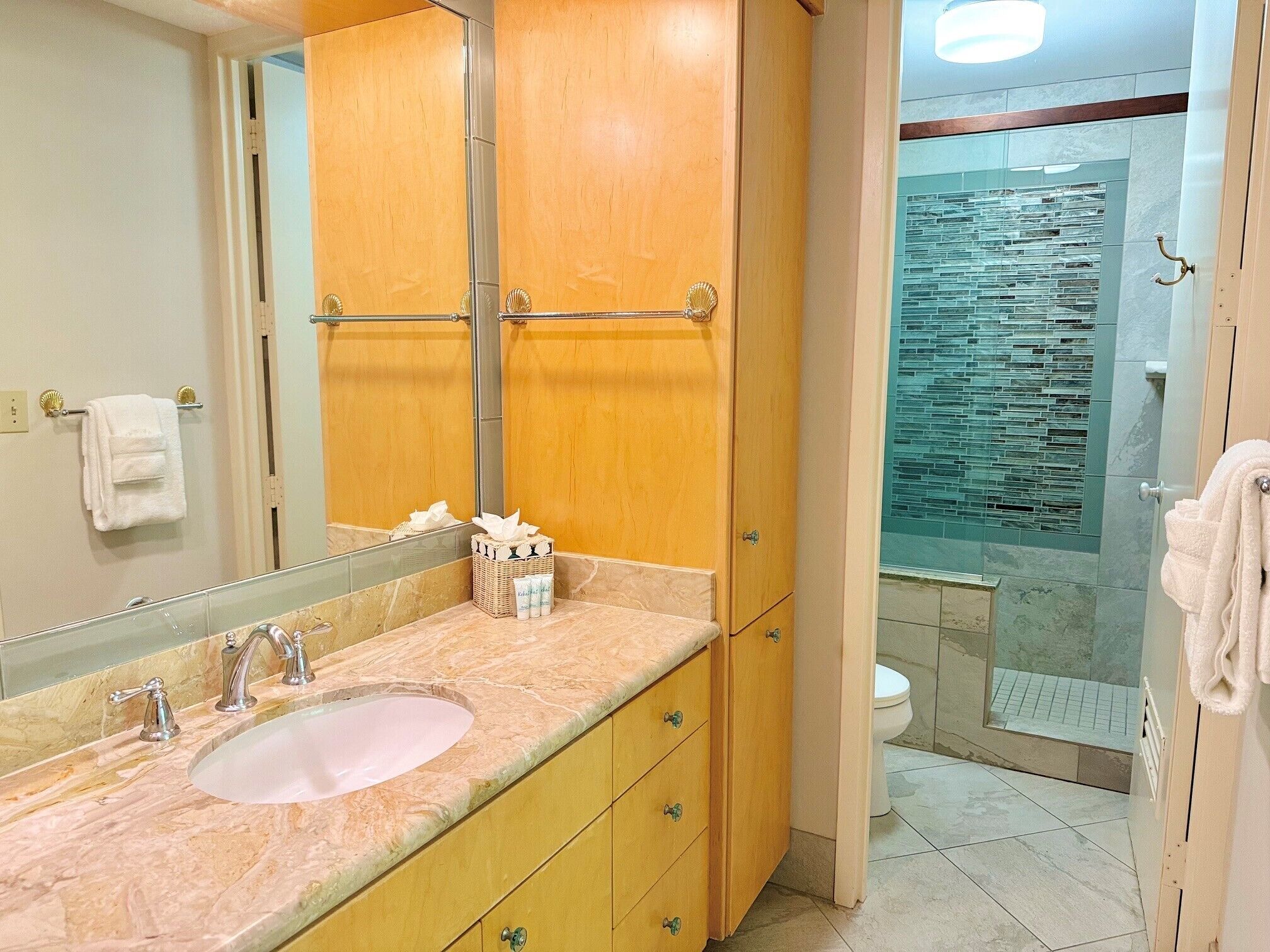 A bathroom with a marble sink, wooden cabinets, a glass shower enclosure, and a toilet.