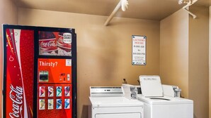 Eine Waschsalon mit einem Coca-Cola Automaten, einem Schild mit den Öffnungszeiten und einem Trockner.