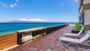 Ein Balkon am Strand mit Liegestühlen, einem Warnschild und Blick auf das Meer.