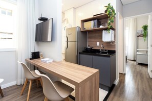 A modern kitchen with a built-in microwave, refrigerator, and sink. There is a wooden dining table with two chairs. - 360 Higienópolis (São Paulo)