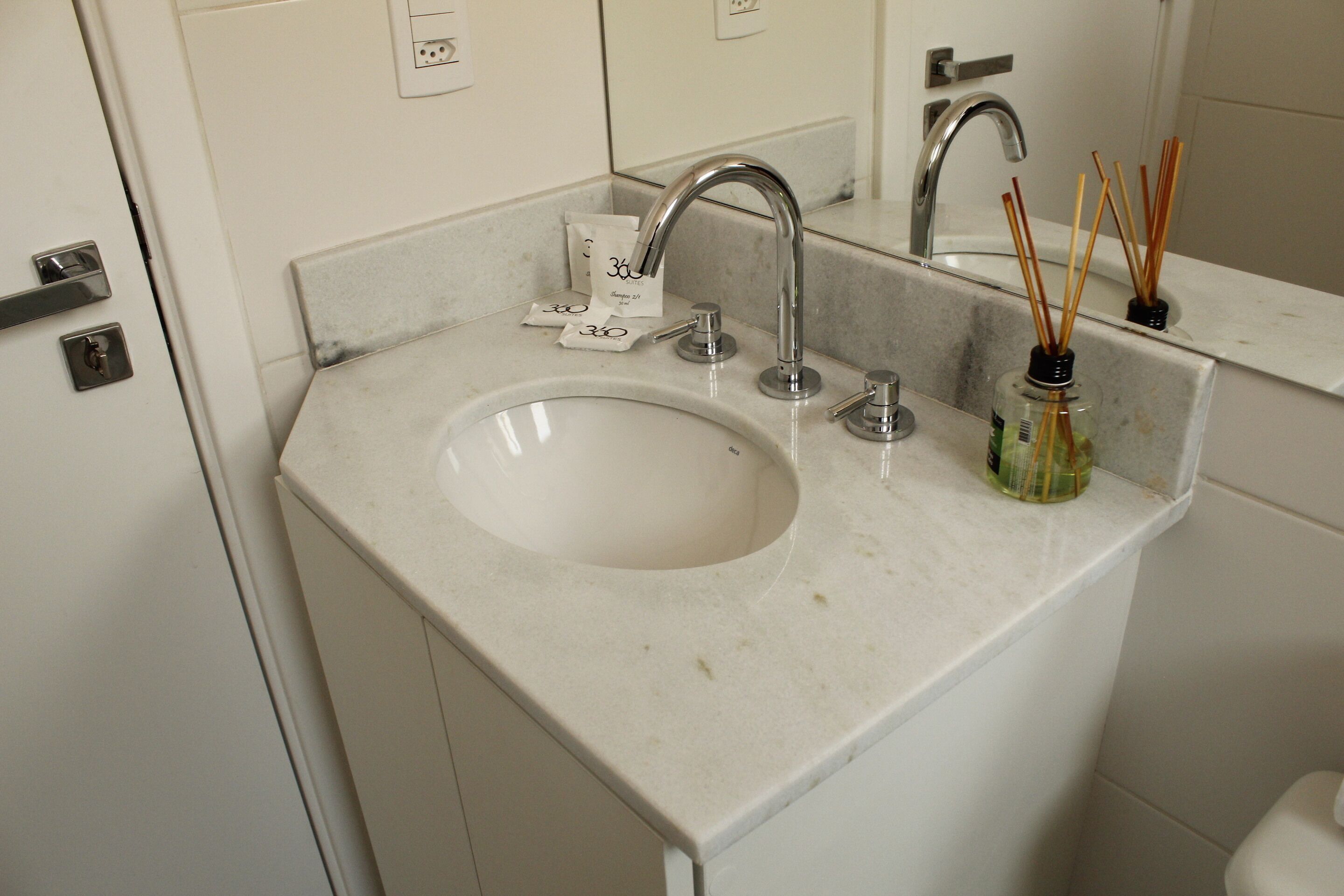 A bathroom sink with a mirror above it, a faucet, and a bottle of reed sticks.