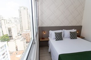 Ein Hotelzimmer mit einem Bett, zwei Nachttischlampen, einem Nachttisch und Blick auf hohe Gebäude.