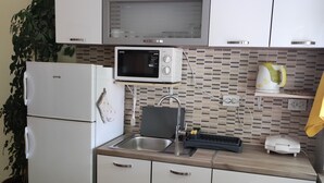 A compact kitchen with a refrigerator, microwave, sink, and a small countertop with a kettle. - Rooms Brezak - Double Room with Shared Kitchen (Lastovo)
