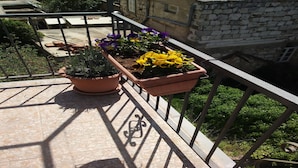 A balcony with two terracotta pots containing plants, a metal railing, and a view of a building in the background. - Rooms Brezak - Double Room with Shared Kitchen (Lastovo)